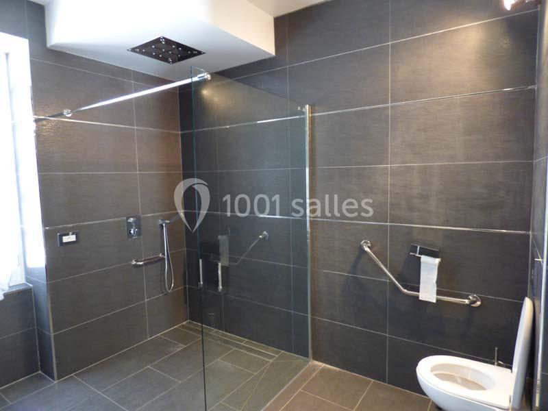 Salle de bain moderne avec douche à l'italienne, barres d'appui, toilettes et carrelage gris foncé.