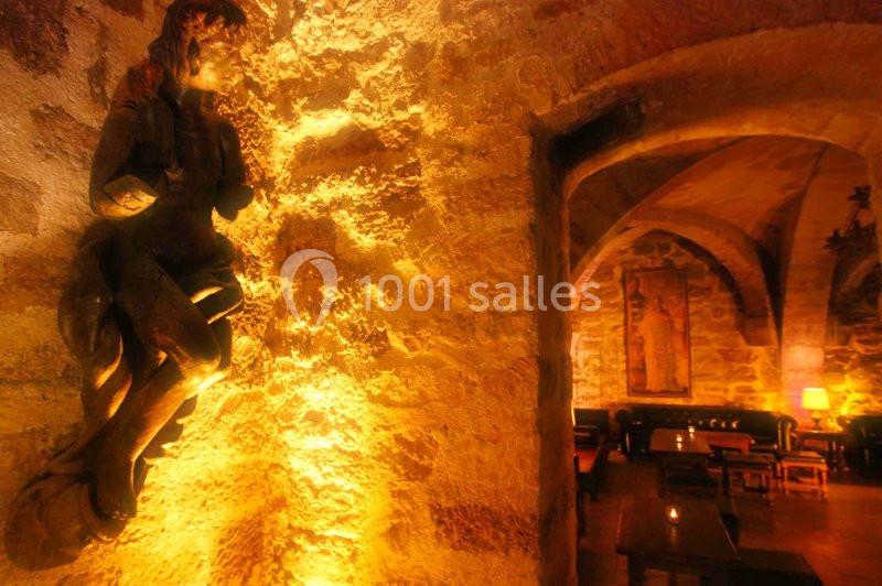 Statue en pierre éclairée dans une salle voûtée en pierre avec des tables et une lumière tamisée.