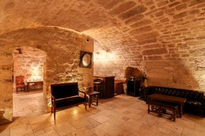 Salle voûtée en pierre éclairée par des lampes et un lustre, avec une table dressée pour un repas.