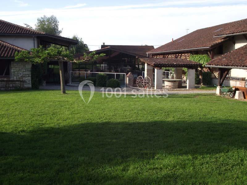 Cour intérieure avec pelouse, puits en pierre, pergola et bâtiments en pierre et bois sous un ciel dégagé.