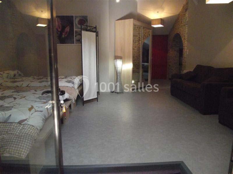 Chambre avec deux lits simples, un canapé, un paravent, et des murs en pierre apparente dans un éclairage doux.