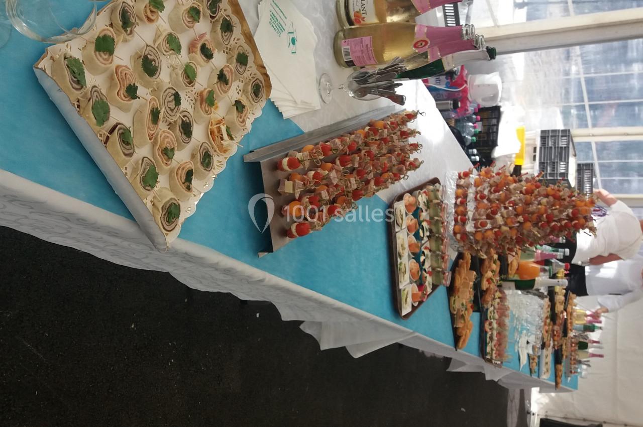 Buffet avec verrines, brochettes et boissons disposés sur une table bleue dans un espace sous tente.