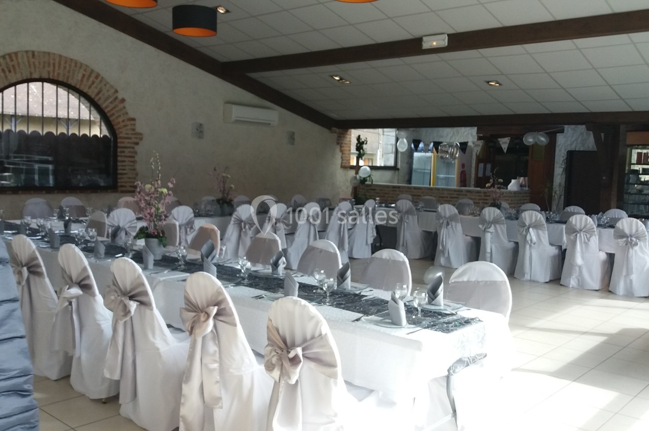 Salle de réception décorée pour un événement, avec des tables dressées et des chaises recouvertes de housses blanches.