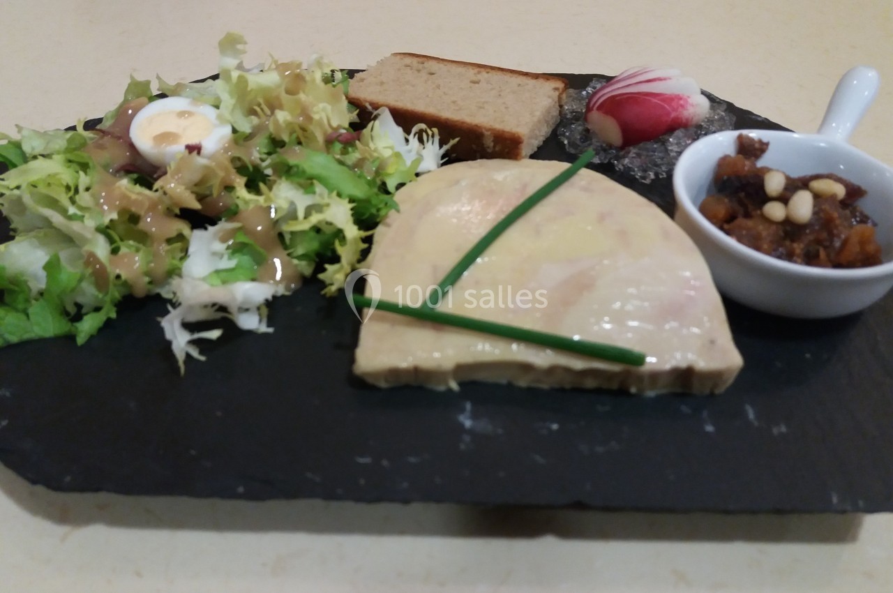 Assiette composée de foie gras, salade verte, pain, radis et chutney dans une coupelle sur une ardoise noire.