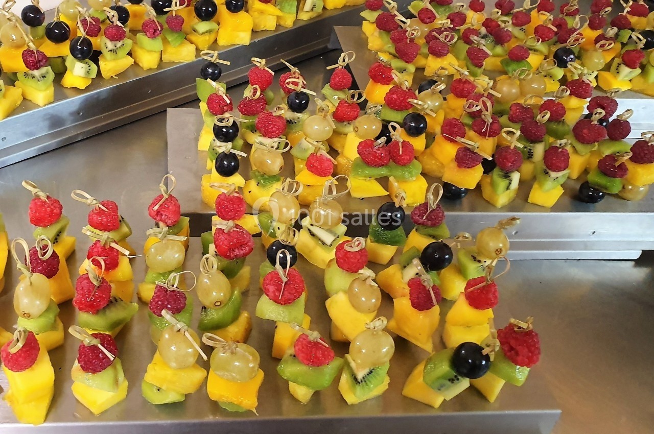 Brochettes de fruits colorées avec raisins, framboises, kiwis, mangues et myrtilles, disposées sur des plateaux en métal.