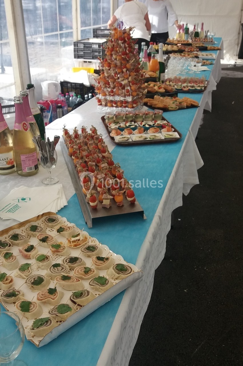 Buffet dressé avec des amuse-bouches variés, boissons et décorations sur une longue table dans une tente blanche.