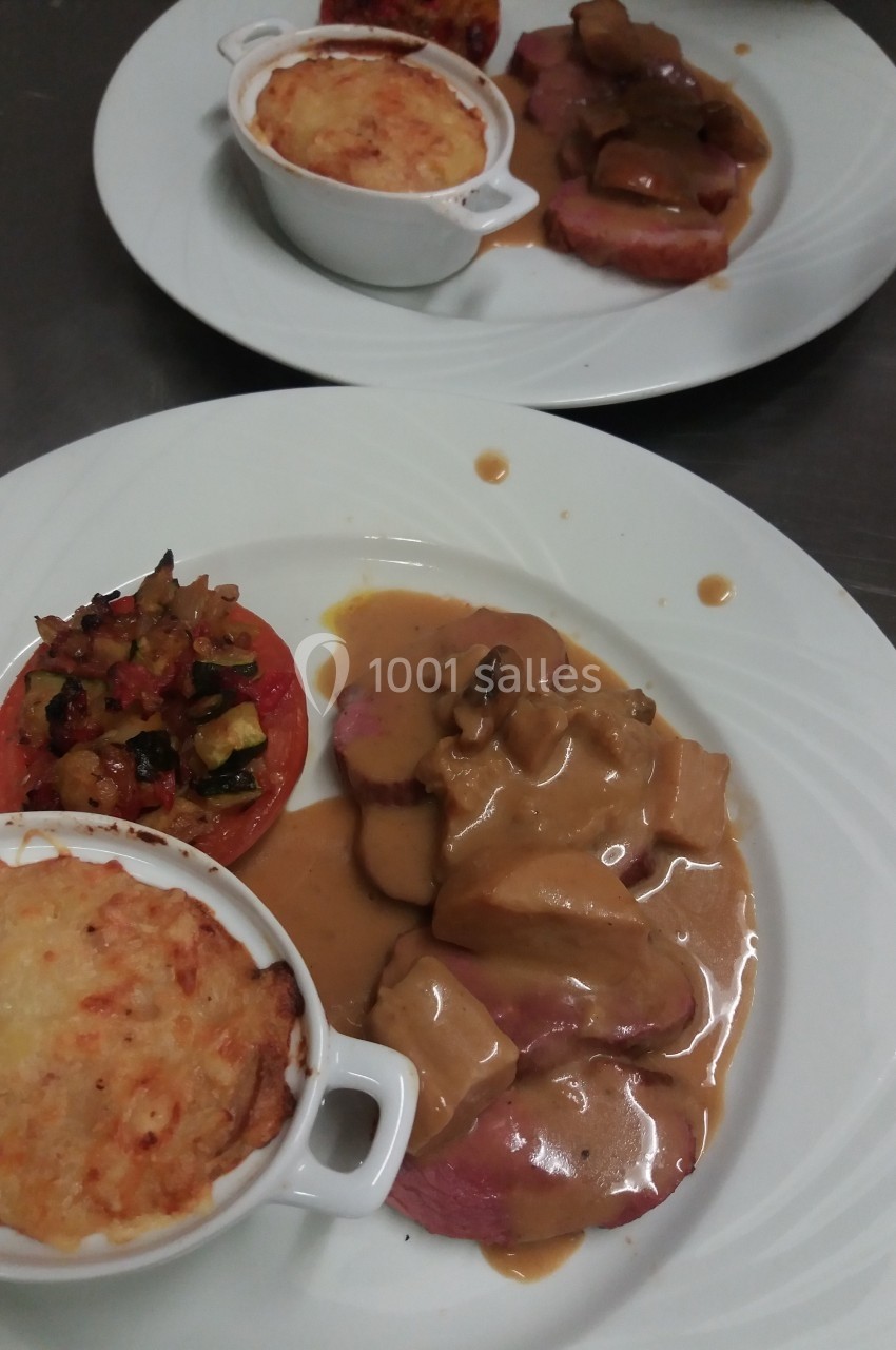 Assiette composée de viande en sauce, gratin individuel, tomate farcie et légumes, servie sur une table.