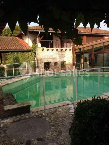 Piscine extérieure entourée d'une barrière de sécurité, située dans une cour avec des bâtiments en pierre et en bois.