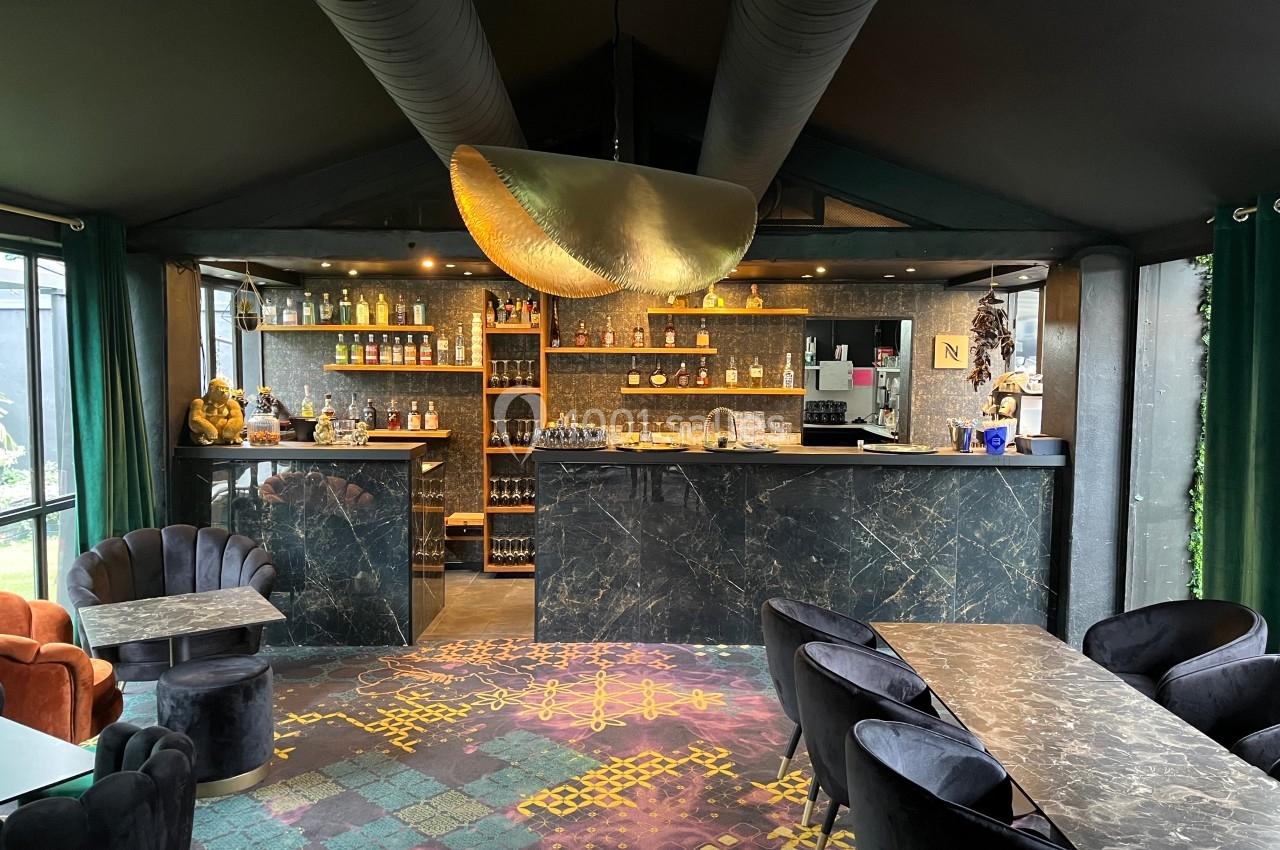 Intérieur d'un bar élégant avec comptoir en marbre sombre, étagères de bouteilles et fauteuils confortables.