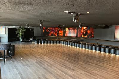 Salle spacieuse avec parquet, murs sombres, éclairage tamisé et écrans affichant des visages colorés.