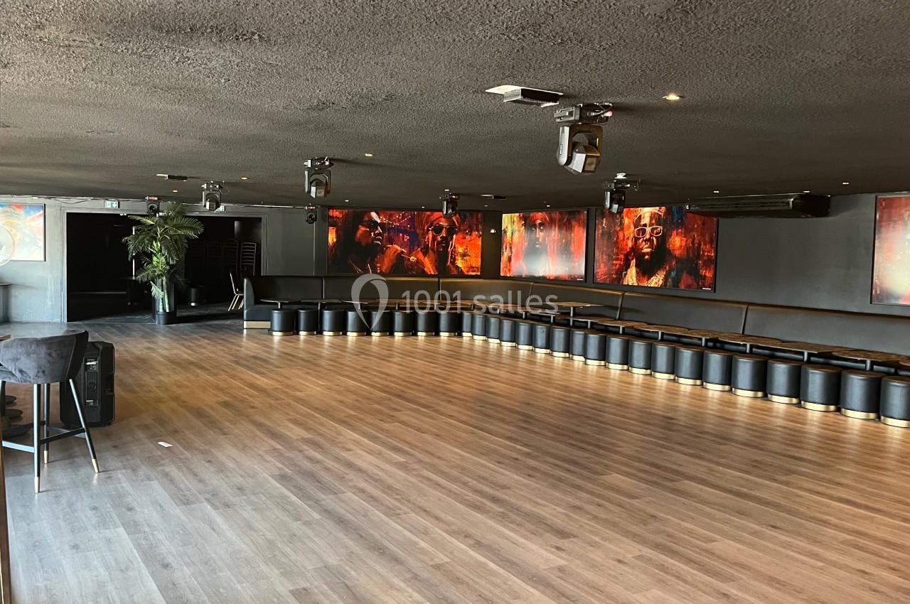 Salle spacieuse avec parquet, murs sombres, éclairage tamisé et écrans affichant des visages colorés.