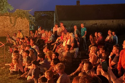 Salon rustique avec murs en pierre, canapés en cuir, table basse et porte ouverte donnant sur un jardin ensoleillé.
