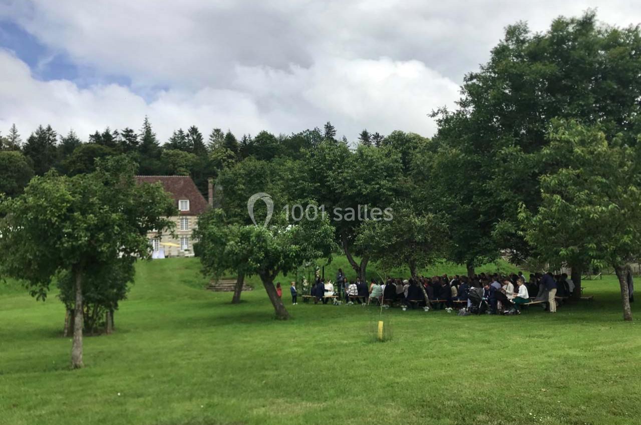 Un groupe de personnes assises en extérieur dans un parc verdoyant près d'une grande maison sous un ciel nuageux.