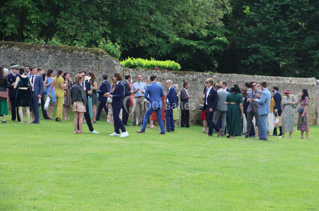 Groupe de personnes discutant en extérieur sur une pelouse, près d'un mur en pierre et entourées de verdure.