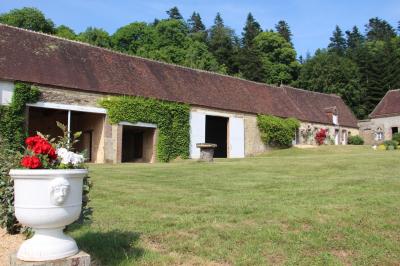Salon rustique avec murs en pierre, canapés en cuir, table basse et porte ouverte donnant sur un jardin ensoleillé.