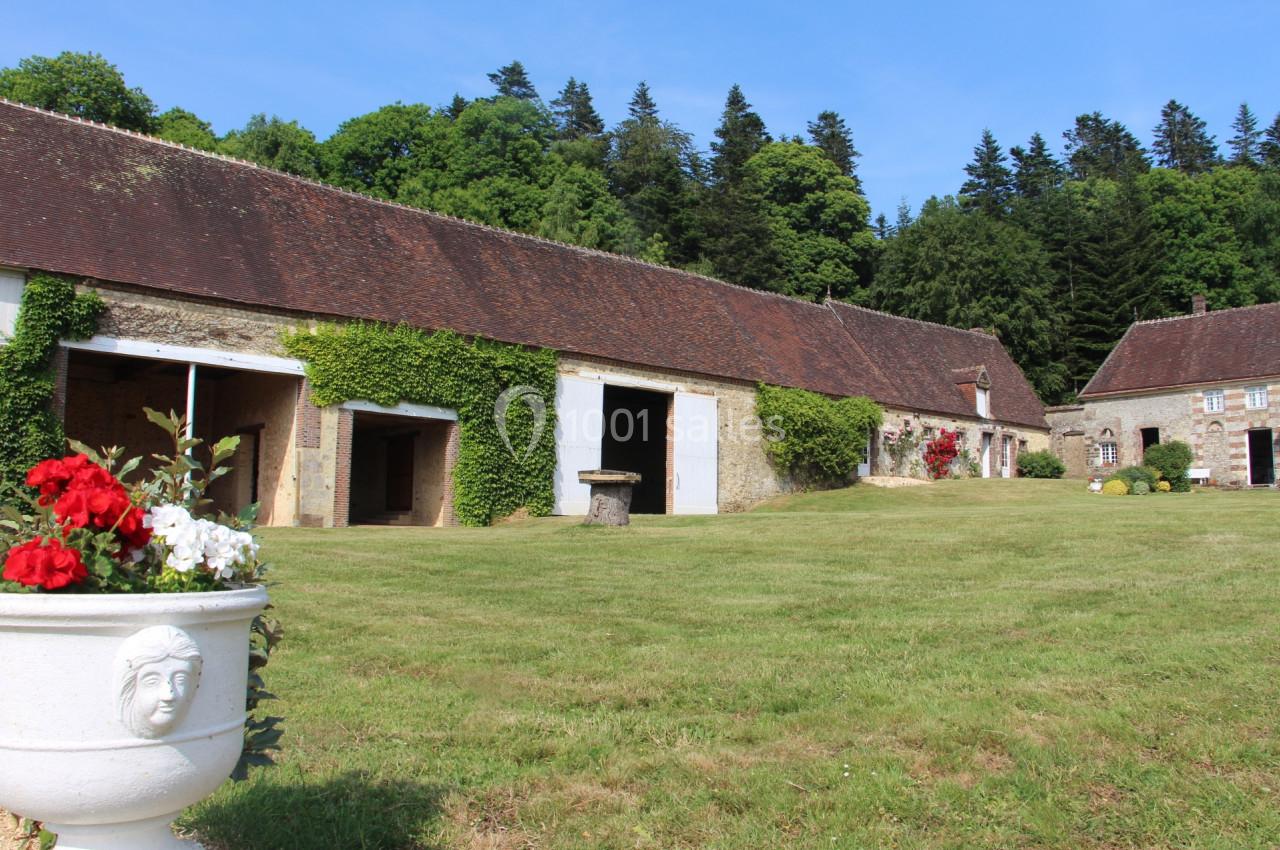 Bâtiments en pierre avec toits en tuiles, entourés de pelouse et de végétation, par une journée ensoleillée.