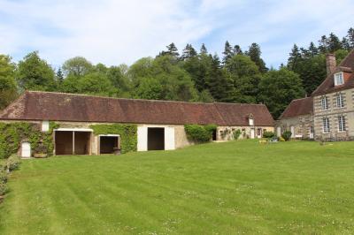 Salon rustique avec murs en pierre, canapés en cuir, table basse et porte ouverte donnant sur un jardin ensoleillé.