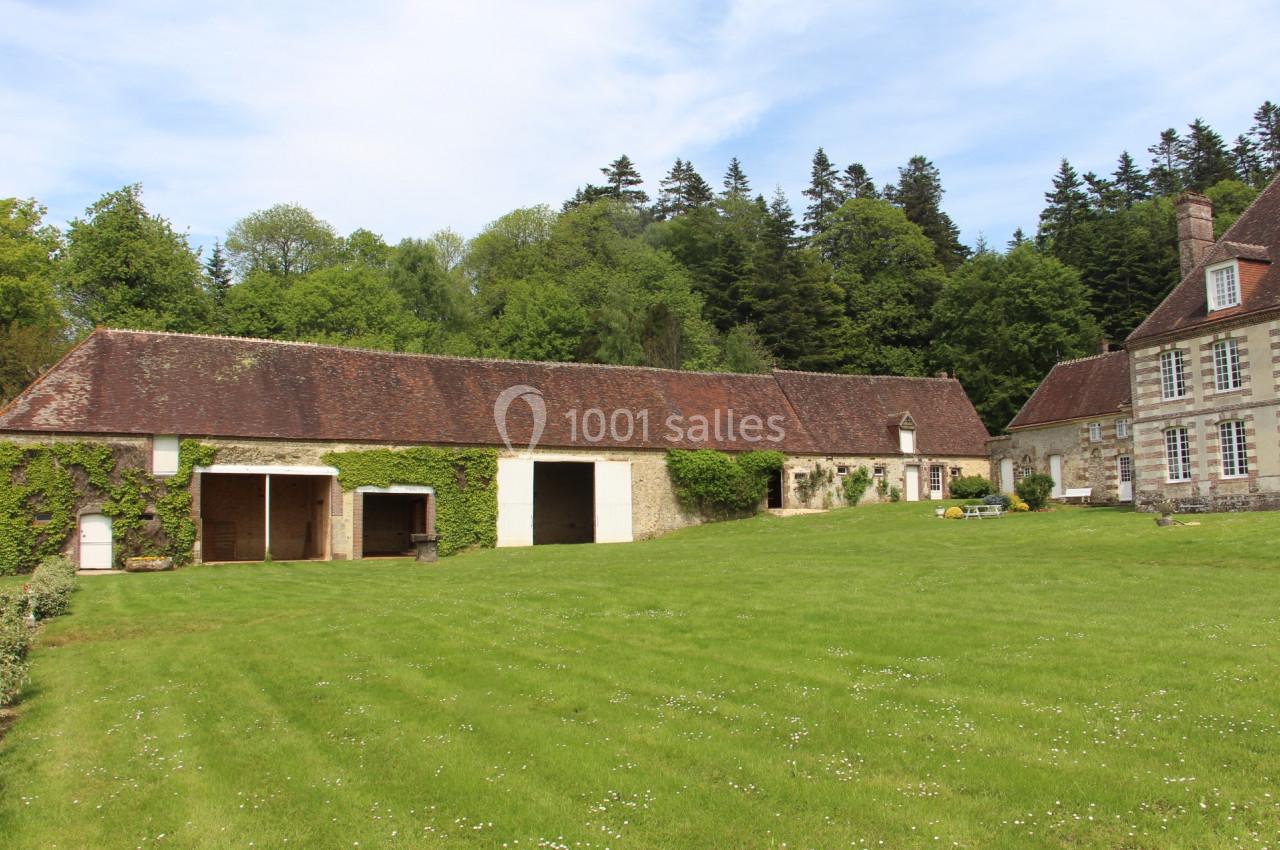 Bâtiments anciens en pierre avec toits en tuiles, entourés d'une pelouse et d'arbres sous un ciel dégagé.