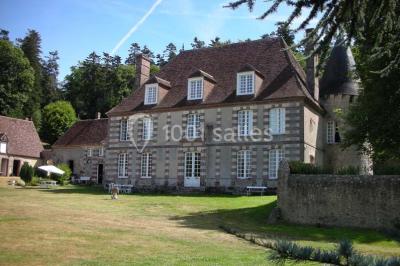 Salon rustique avec murs en pierre, canapés en cuir, table basse et porte ouverte donnant sur un jardin ensoleillé.