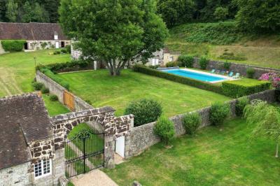 Salon rustique avec murs en pierre, canapés en cuir, table basse et porte ouverte donnant sur un jardin ensoleillé.