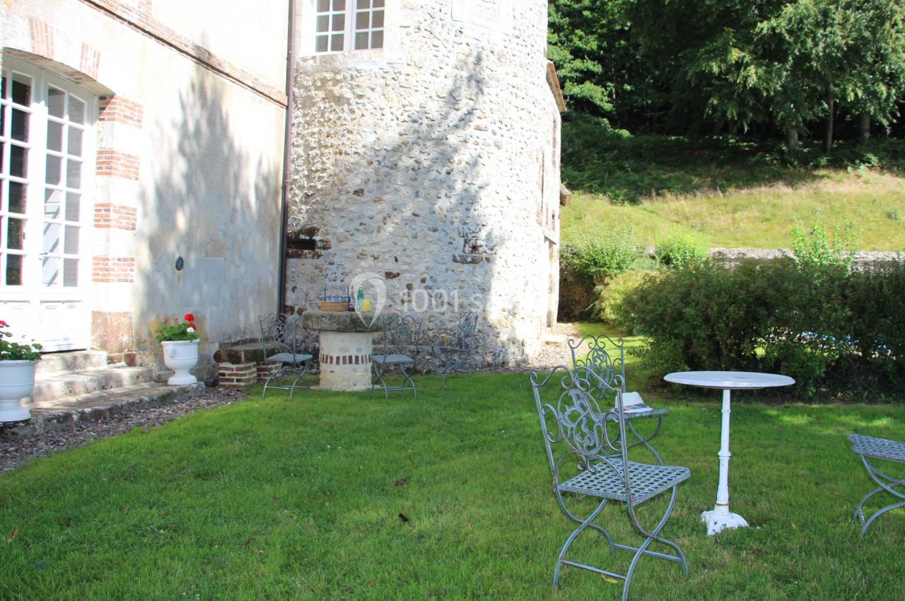 Mobilier de jardin en fer forgé sur une pelouse, près d'une maison en pierre et d'un mur végétalisé.