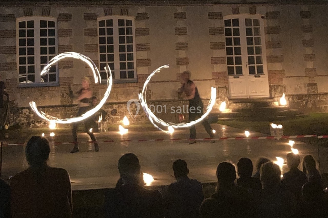 Deux artistes réalisent un spectacle de jonglage avec du feu devant un bâtiment en pierre, de nuit.