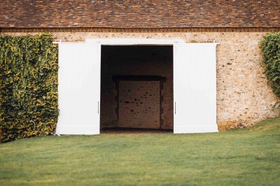 Salon rustique avec murs en pierre, canapés en cuir, table basse et porte ouverte donnant sur un jardin ensoleillé.
