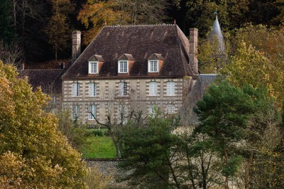 Salon rustique avec murs en pierre, canapés en cuir, table basse et porte ouverte donnant sur un jardin ensoleillé.