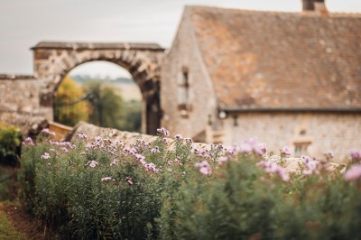 Salon rustique avec murs en pierre, canapés en cuir, table basse et porte ouverte donnant sur un jardin ensoleillé.