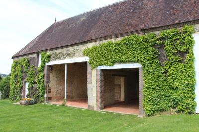 Salon rustique avec murs en pierre, canapés en cuir, table basse et porte ouverte donnant sur un jardin ensoleillé.