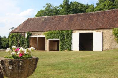Salon rustique avec murs en pierre, canapés en cuir, table basse et porte ouverte donnant sur un jardin ensoleillé.