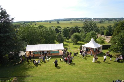 Salon rustique avec murs en pierre, canapés en cuir, table basse et porte ouverte donnant sur un jardin ensoleillé.