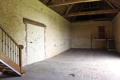 Salon rustique avec murs en pierre, canapés en cuir, table basse et porte ouverte donnant sur un jardin ensoleillé.