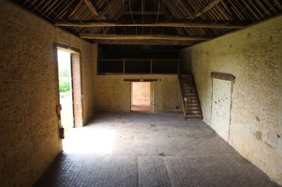 Salon rustique avec murs en pierre, canapés en cuir, table basse et porte ouverte donnant sur un jardin ensoleillé.