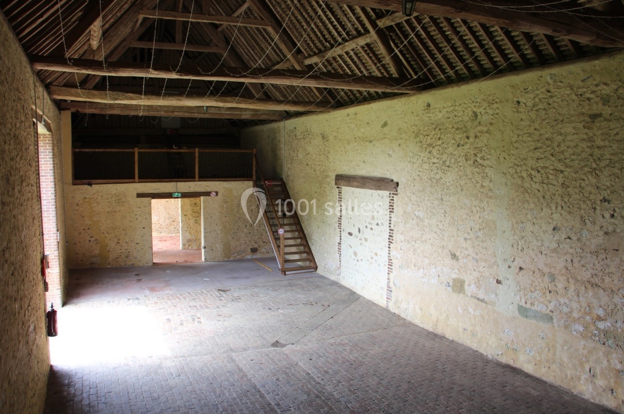 Intérieur d'une grange en pierre avec un sol en briques, un escalier en bois et une mezzanine.