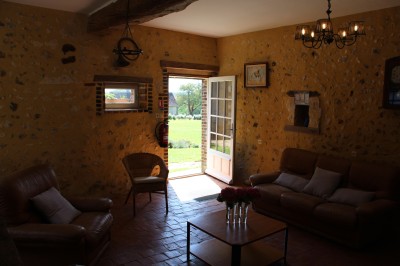 Salon rustique avec murs en pierre, canapés en cuir, table basse et porte ouverte donnant sur un jardin ensoleillé.