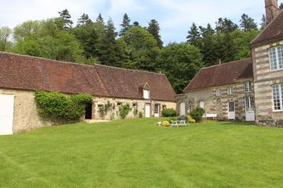 Salon rustique avec murs en pierre, canapés en cuir, table basse et porte ouverte donnant sur un jardin ensoleillé.