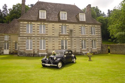 Salon rustique avec murs en pierre, canapés en cuir, table basse et porte ouverte donnant sur un jardin ensoleillé.