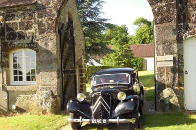 Salon rustique avec murs en pierre, canapés en cuir, table basse et porte ouverte donnant sur un jardin ensoleillé.