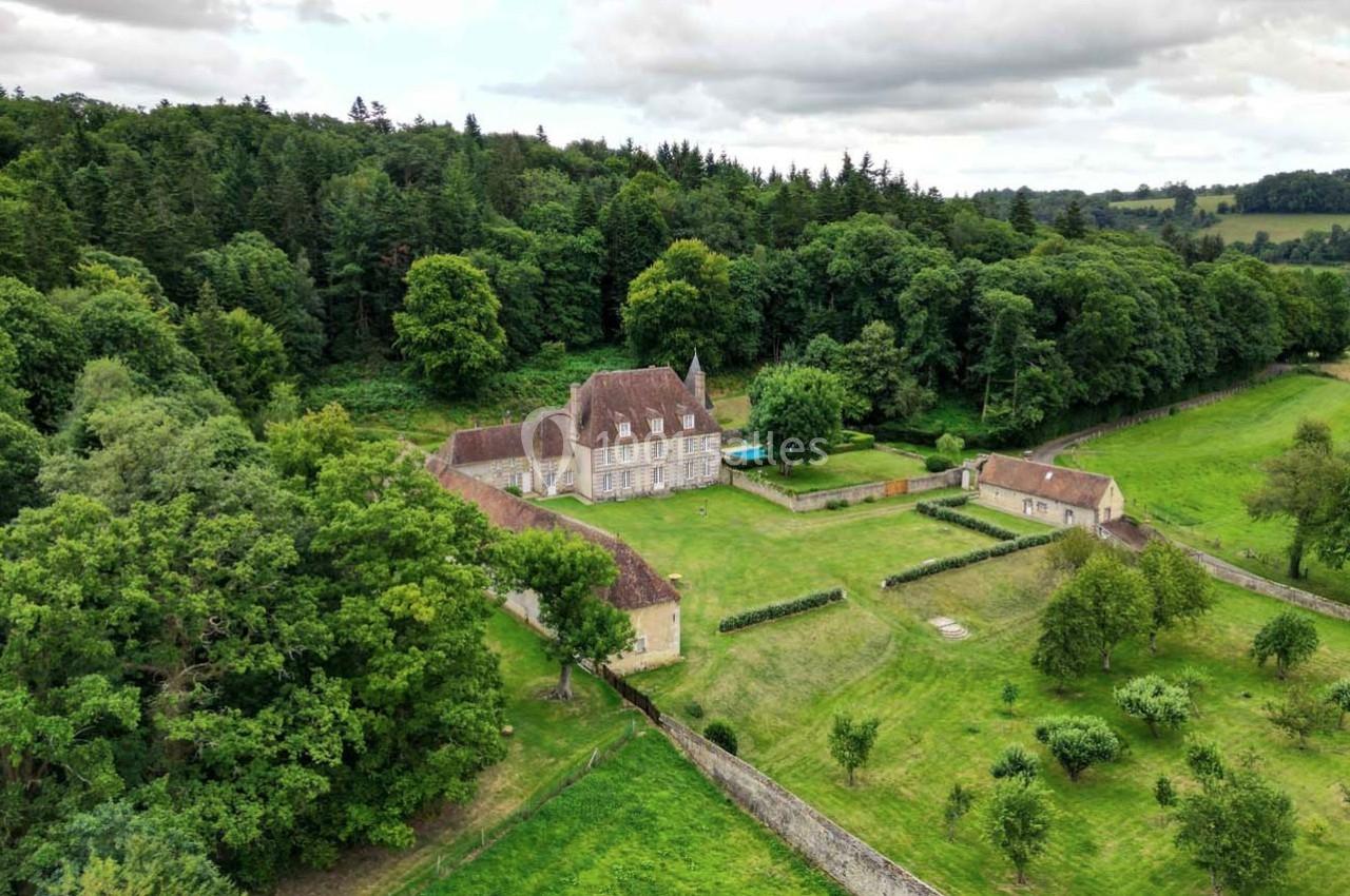 Vue aérienne d'un domaine avec un manoir entouré de jardins, de murs en pierre et d'une forêt dense.