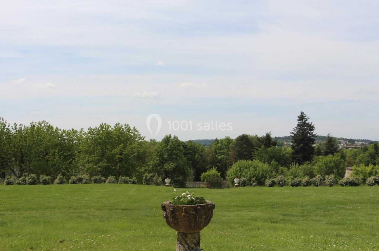 Vasque en pierre avec des plantes, placée sur une pelouse verdoyante entourée d'arbres sous un ciel dégagé.