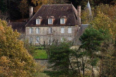 Salon rustique avec murs en pierre, canapés en cuir, table basse et porte ouverte donnant sur un jardin ensoleillé.