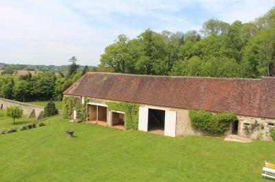 Salon rustique avec murs en pierre, canapés en cuir, table basse et porte ouverte donnant sur un jardin ensoleillé.
