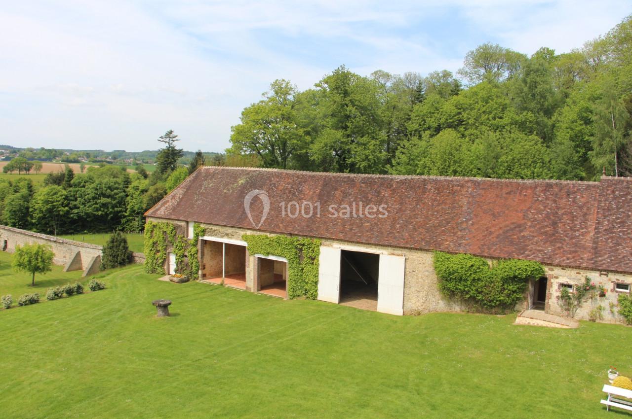 Bâtiment en pierre avec toit en tuiles, entouré de pelouse et d'arbres, sous un ciel dégagé.