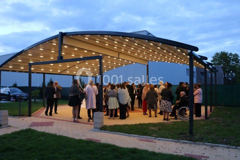 Groupe de personnes rassemblées sous un abri éclairé en soirée, près d'un bâtiment industriel.