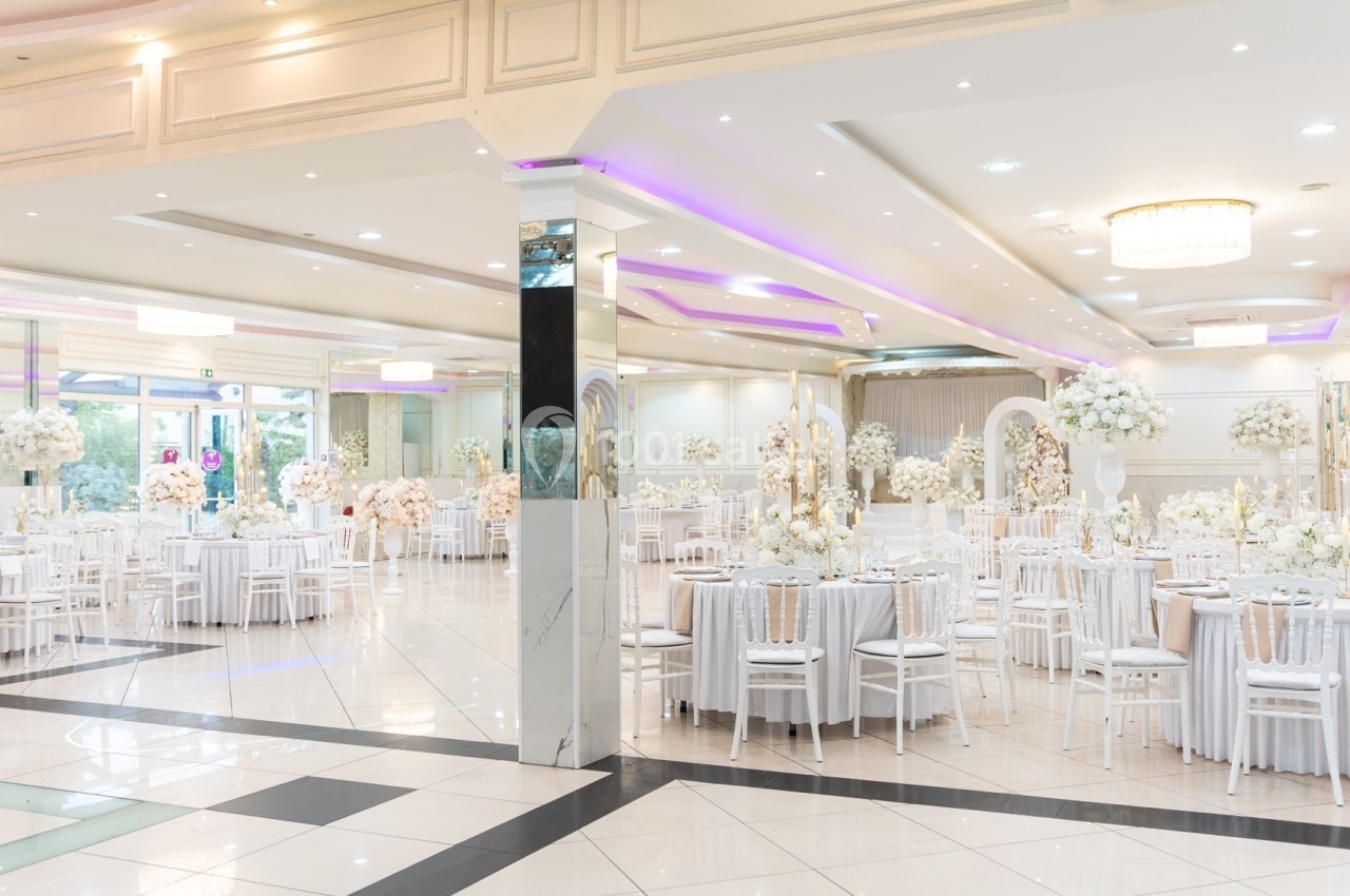 Salle de réception lumineuse décorée de tables rondes avec nappes blanches, chaises assorties et arrangements floraux.