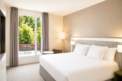 Miniature Location salle Meudon (Hauts-de-Seine) - L'Ermitage #29 Chambre lumineuse avec un grand lit, des rideaux gris, une table basse et une vue sur un balcon avec végétation.