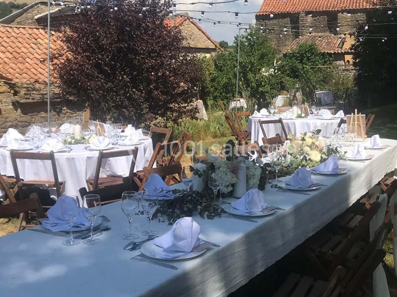 Tables de réception décorées avec nappes blanches, fleurs et vaisselle, installées en extérieur sous des guirlandes…