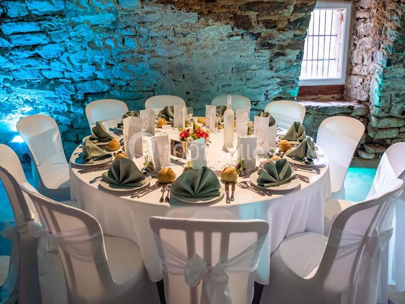 Table ronde élégamment dressée avec nappes blanches, serviettes pliées, couverts et décorations florales dans une salle en…