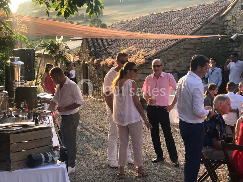 Groupe de personnes discutant près d'une table de buffet en extérieur, devant des bâtiments en pierre sous une lumière de…